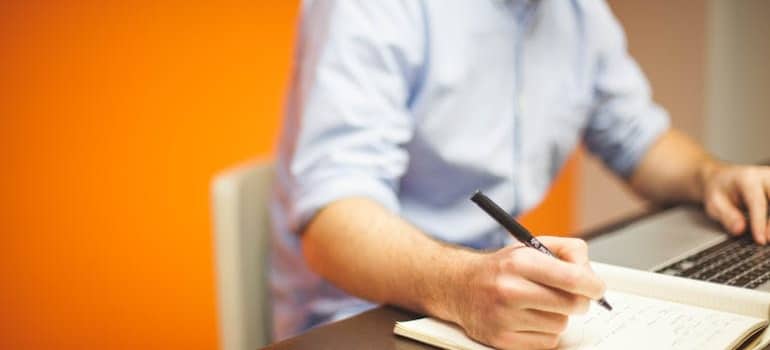 A businessman writing in a notebook a plan so he can prepare for an office move.